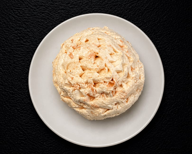 A creamy, light orange cheese ball with visible chunks of cheese, served on a white plate.